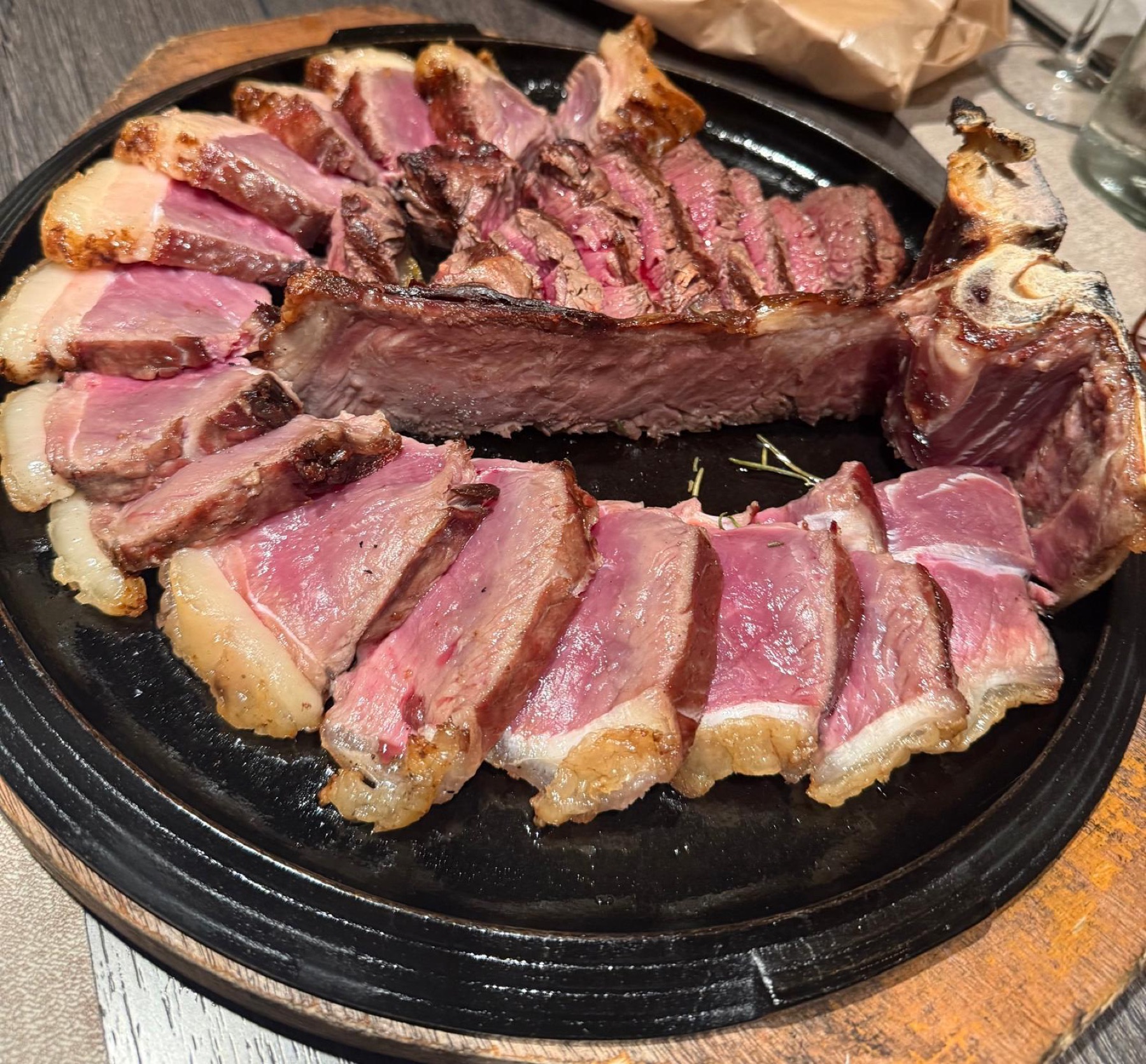 Carne alla griglia servita in tavola, con un bicchiere di vino sullo sfondo.