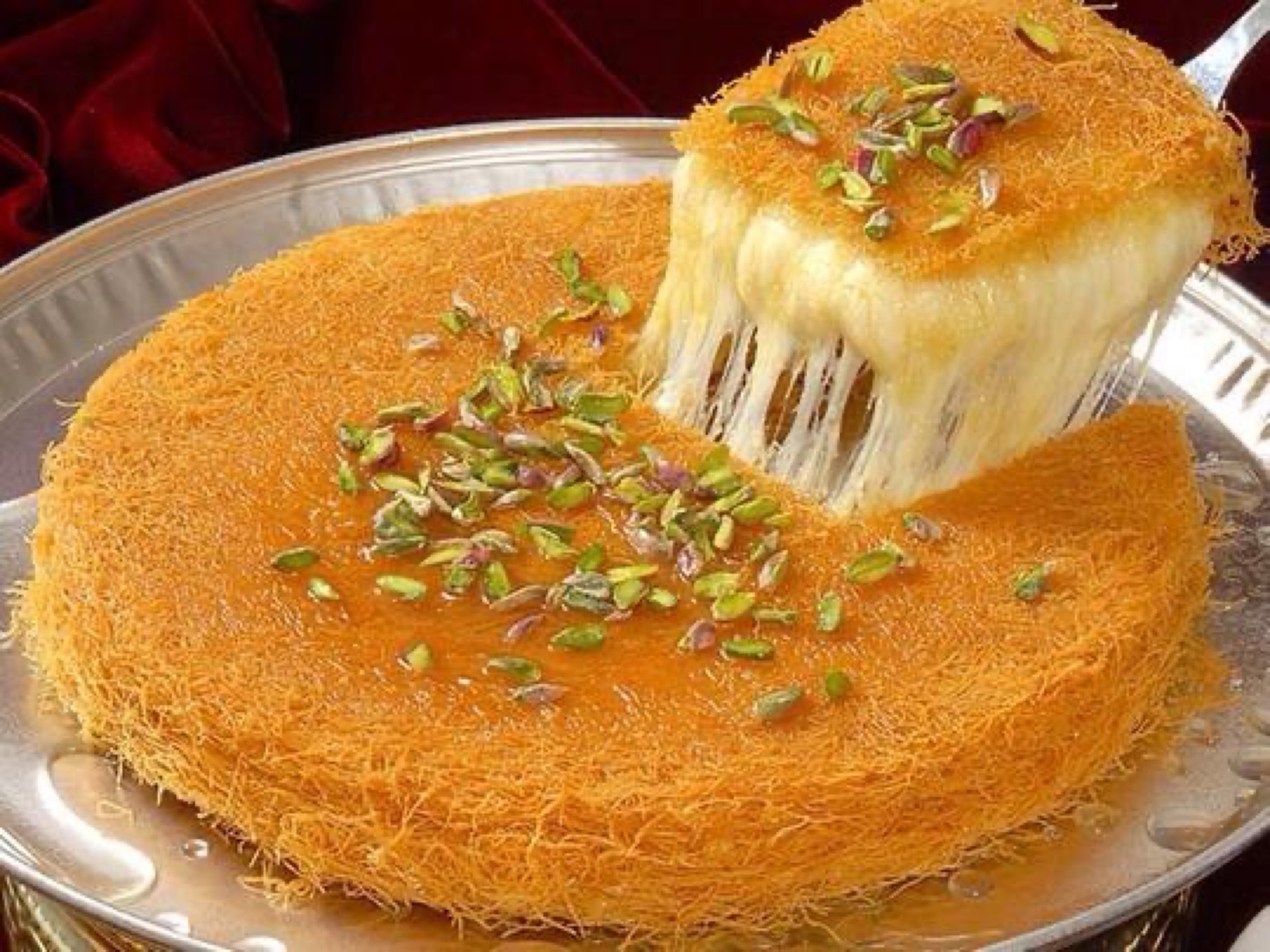 Kunafa calda con pistacchio tritato, il filo di formaggio filante in primo piano.