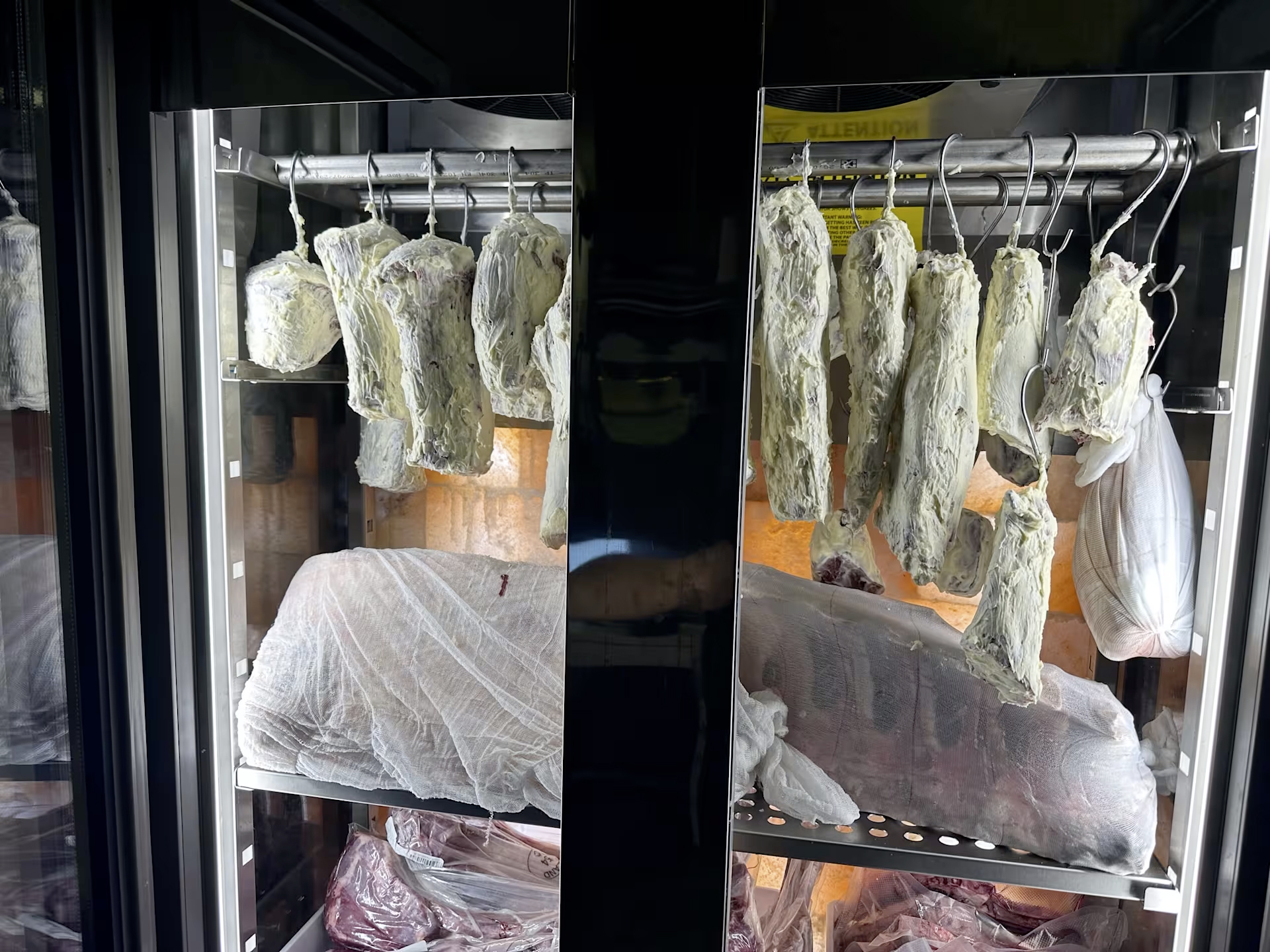 Carne frollata in casa, servita in tavola davanti alla vetrina di frollatura.