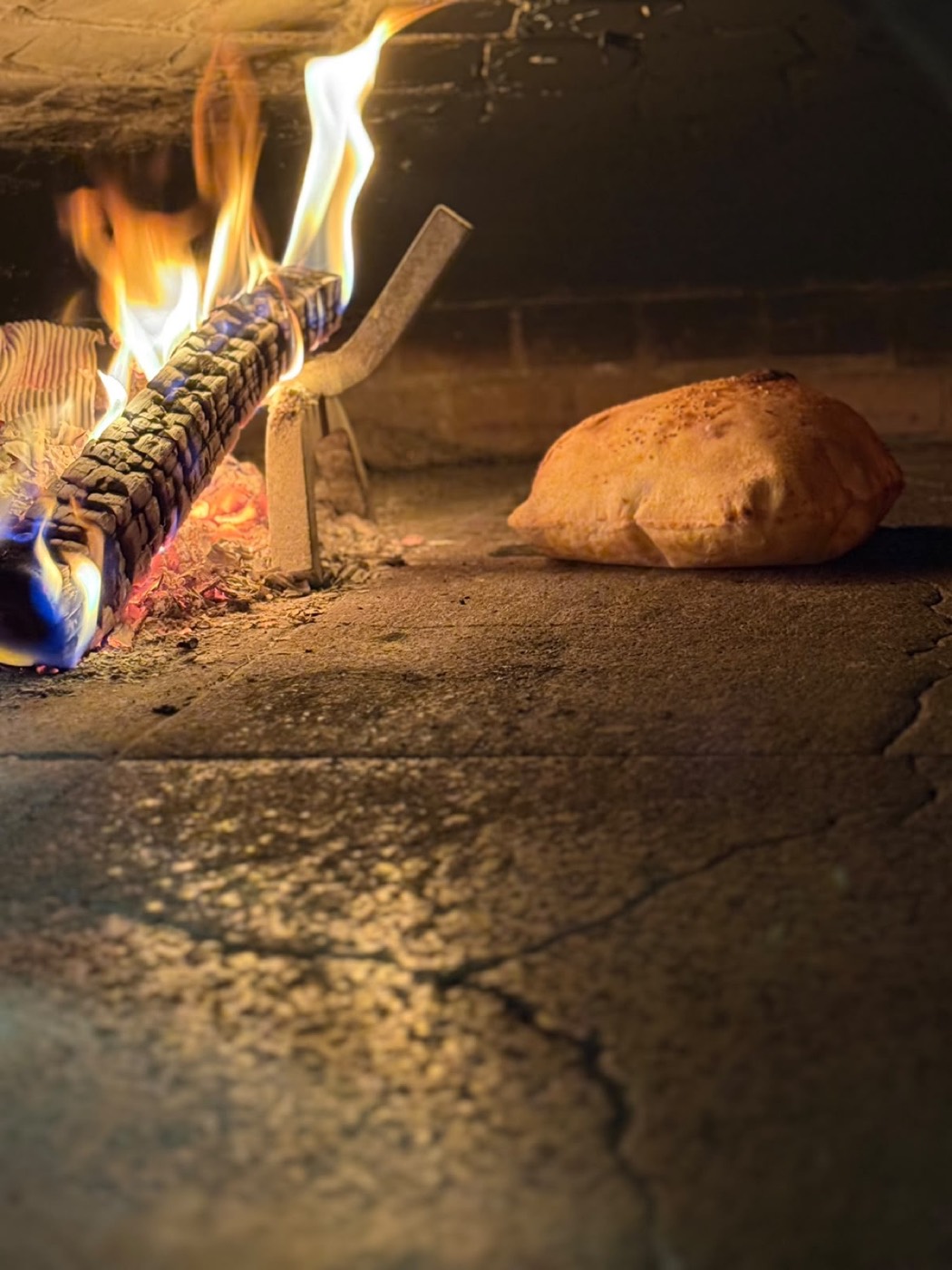 Pane arabo appena infornato, con il forno a legna acceso sullo sfondo.